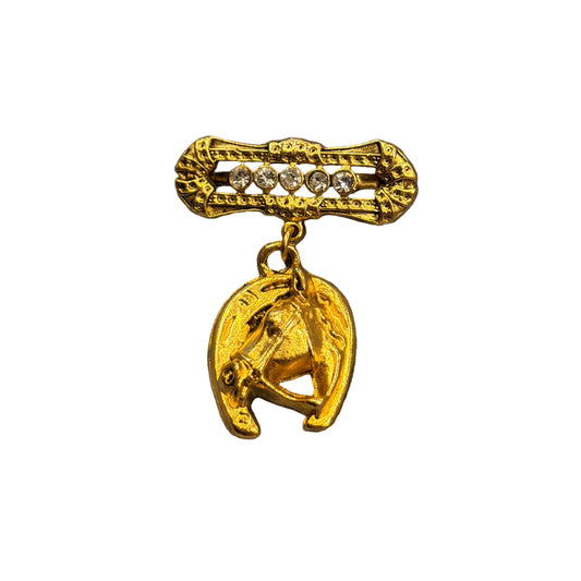 A gold-toned horse-themed brooch featuring a dangling horse charm and a bar with small clear rhinestones, displayed on a gray textured faux fur surface.