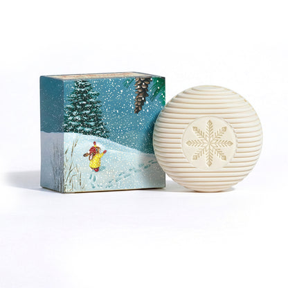First Snowfall in the Pines large gift soap - round snowflake-embossed bar soap beside its illustrated snowy pine forest gift box