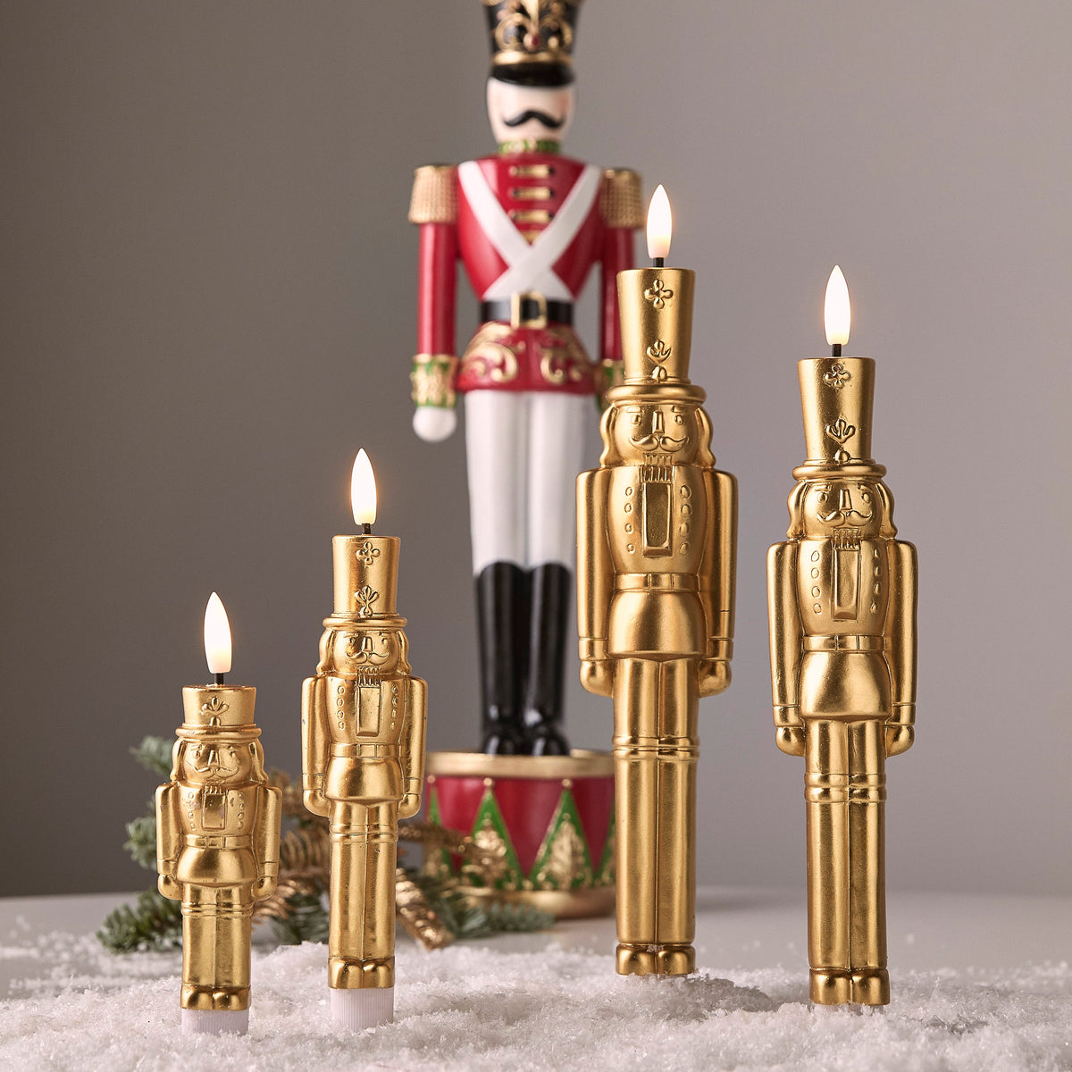 Gold nutcracker flameless taper candles lit on a snowy Christmas display