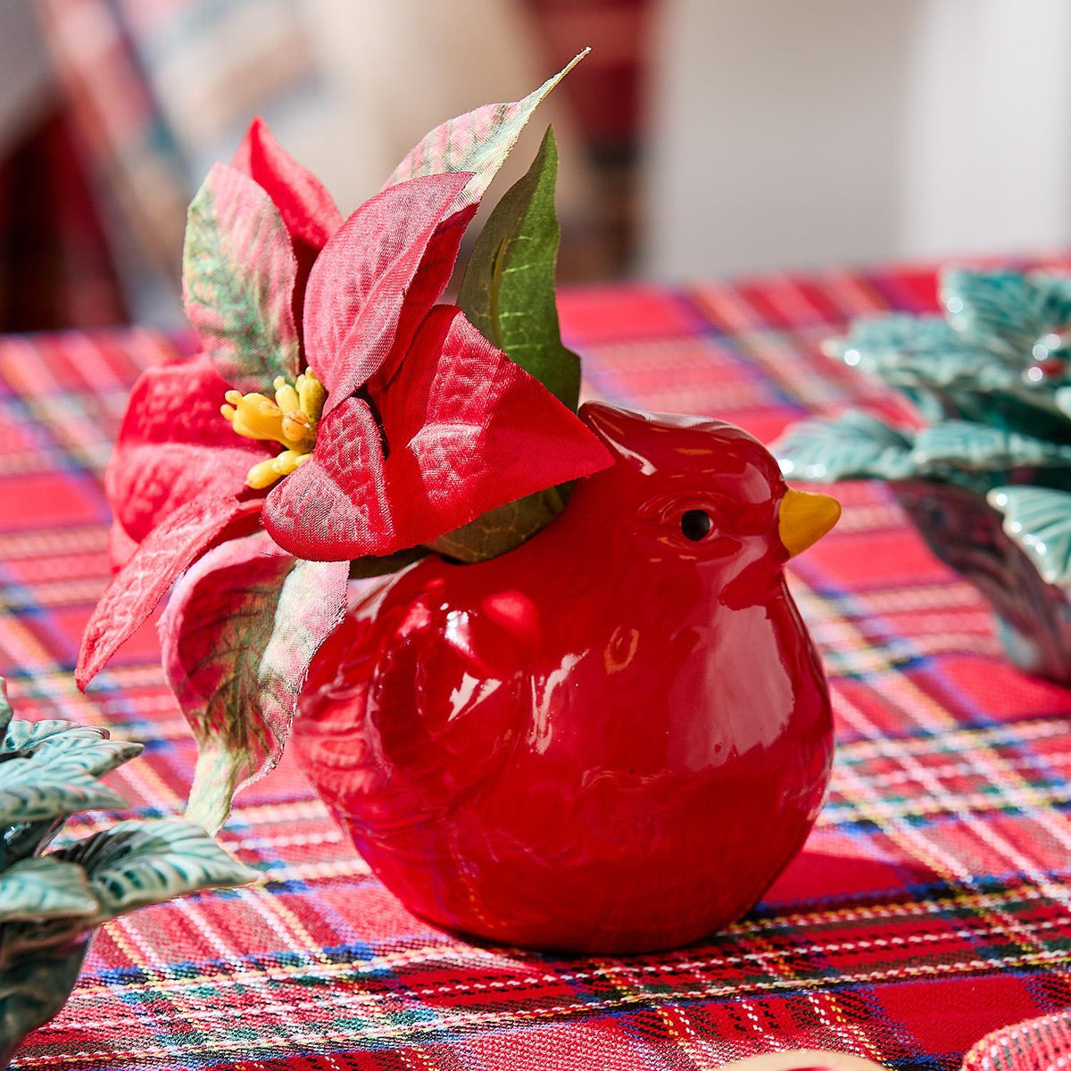 Red ceramic cardinal used as a bud vase with poinsettia on a plaid holiday table