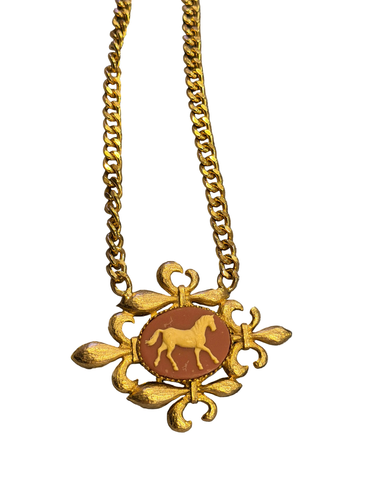 A gold-tone chain necklace with a decorative pendant featuring a brown oval centerpiece with a gold horse silhouette, displayed on a textured gray fabric background.